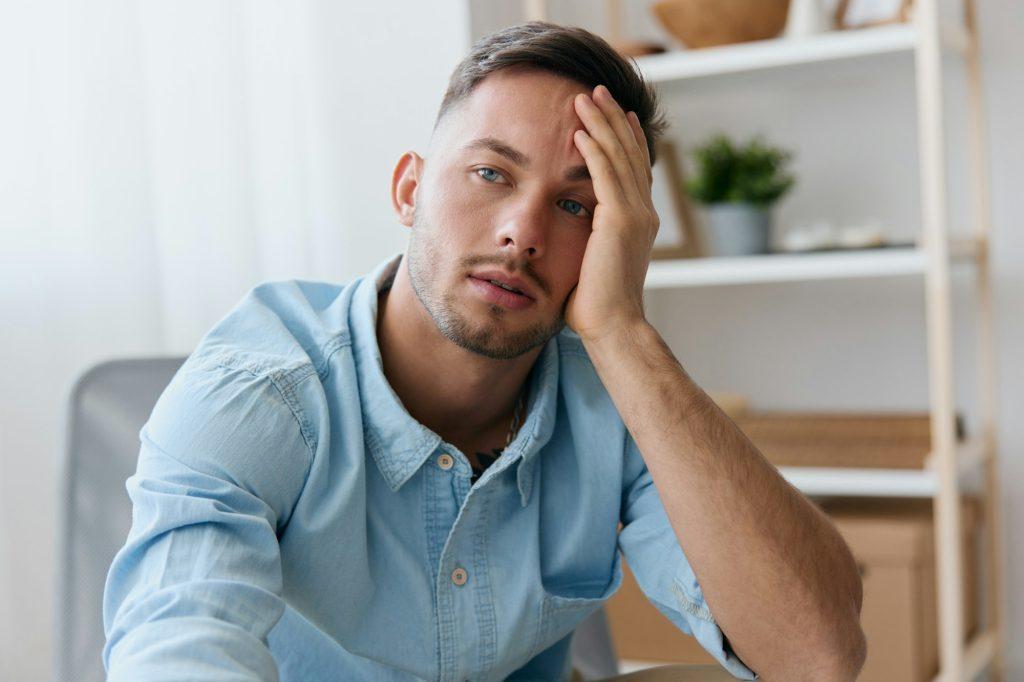 Sad frustrated young man reclines on hand looks aside think about difficult life decision bad news